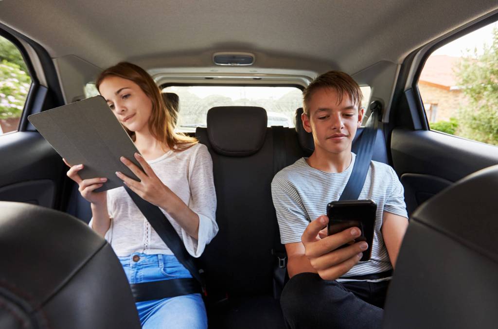 Foto f von Jugendlichen auf dem Rücksitz eines Autos, die auf ihre mobilen Geräte schauen.