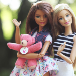 Two Barbie dolls holding a teddy